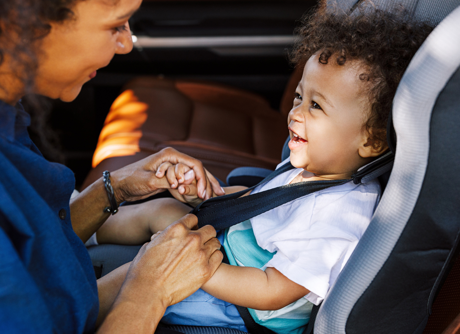 Lady holding the hands of a child who is sitting in an infant car seat