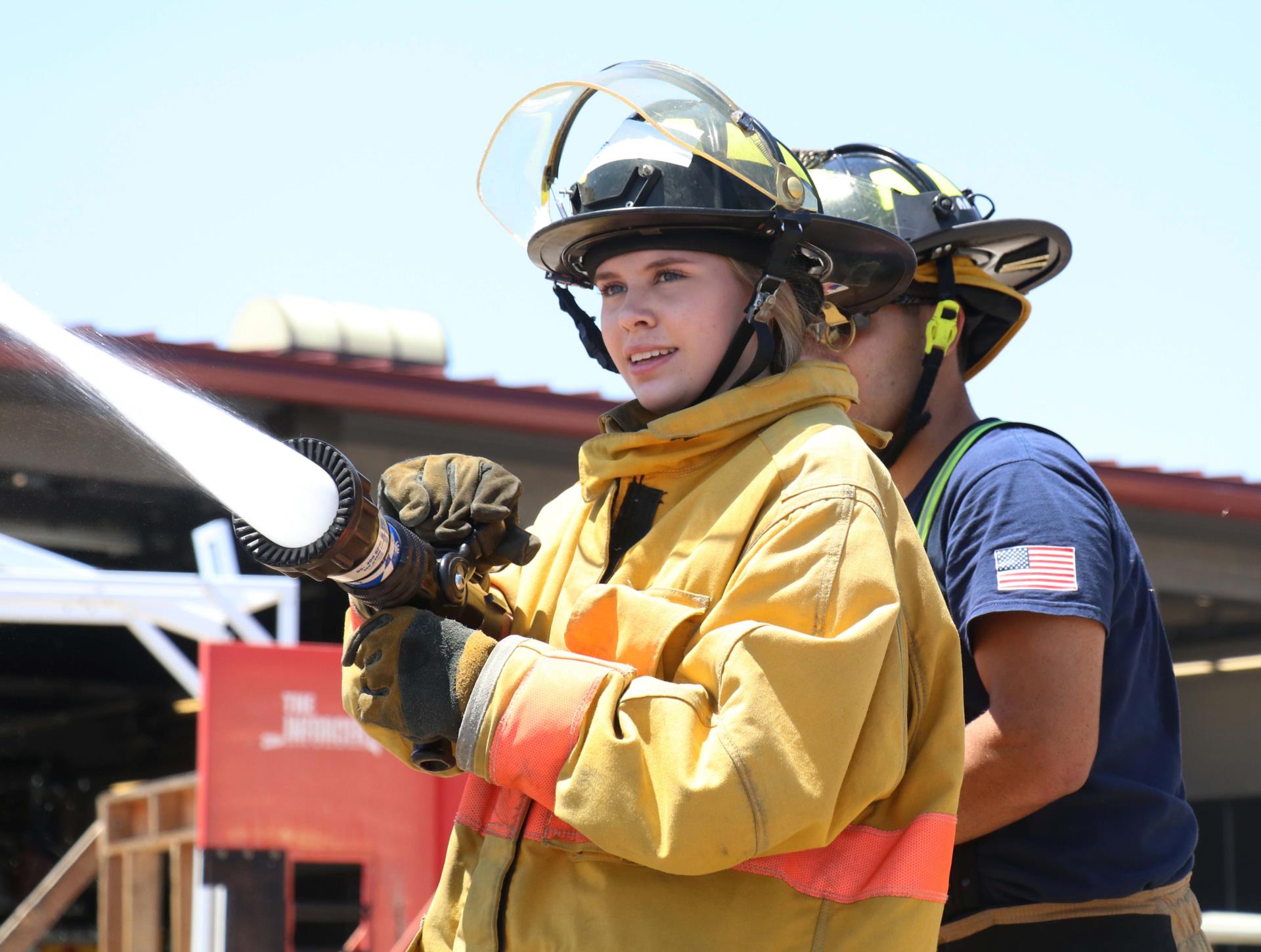 Young female in firefighter gear spraying water out of fire hose