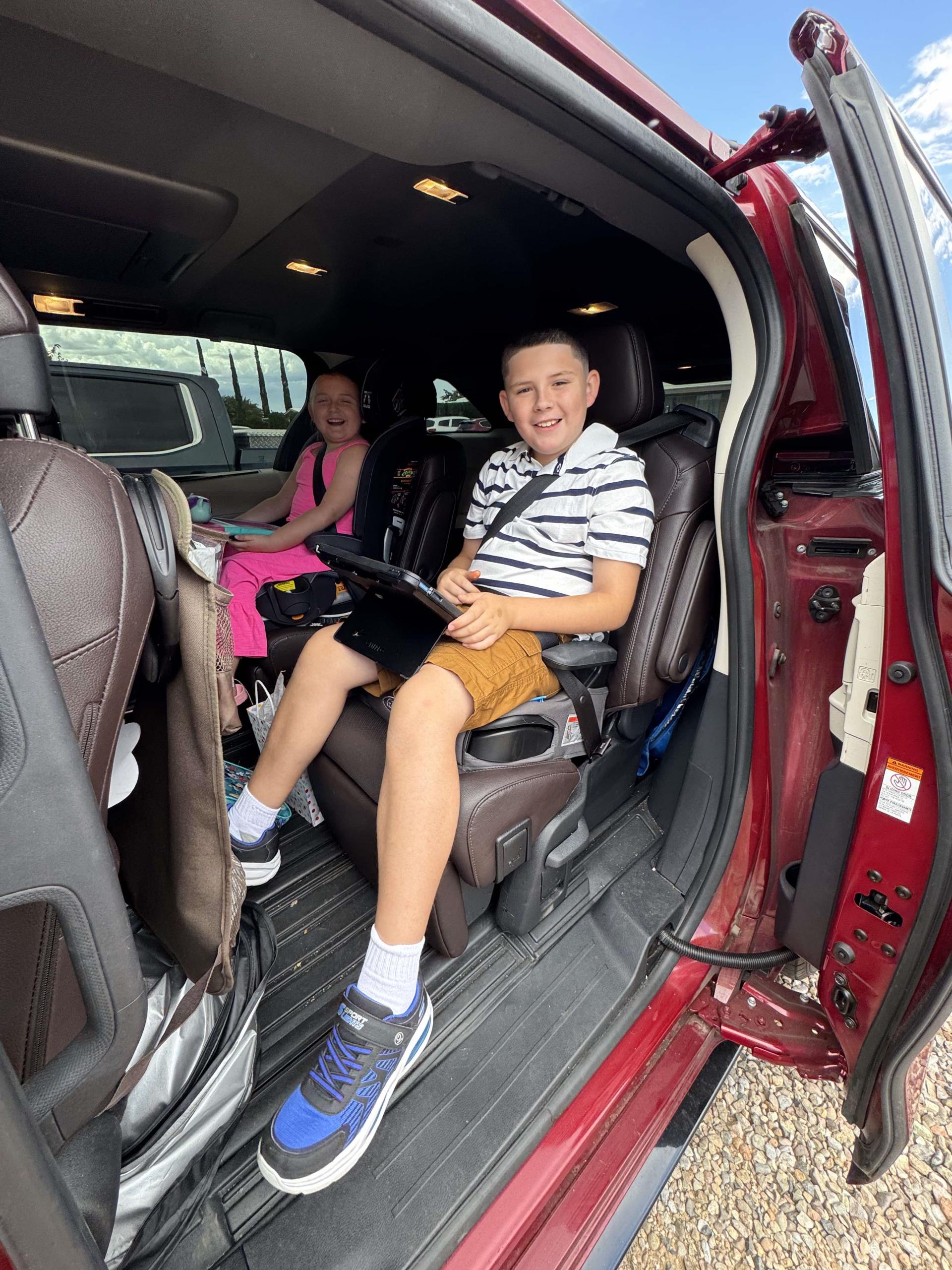 A young boy and girl sit in child car safety seats, smiling