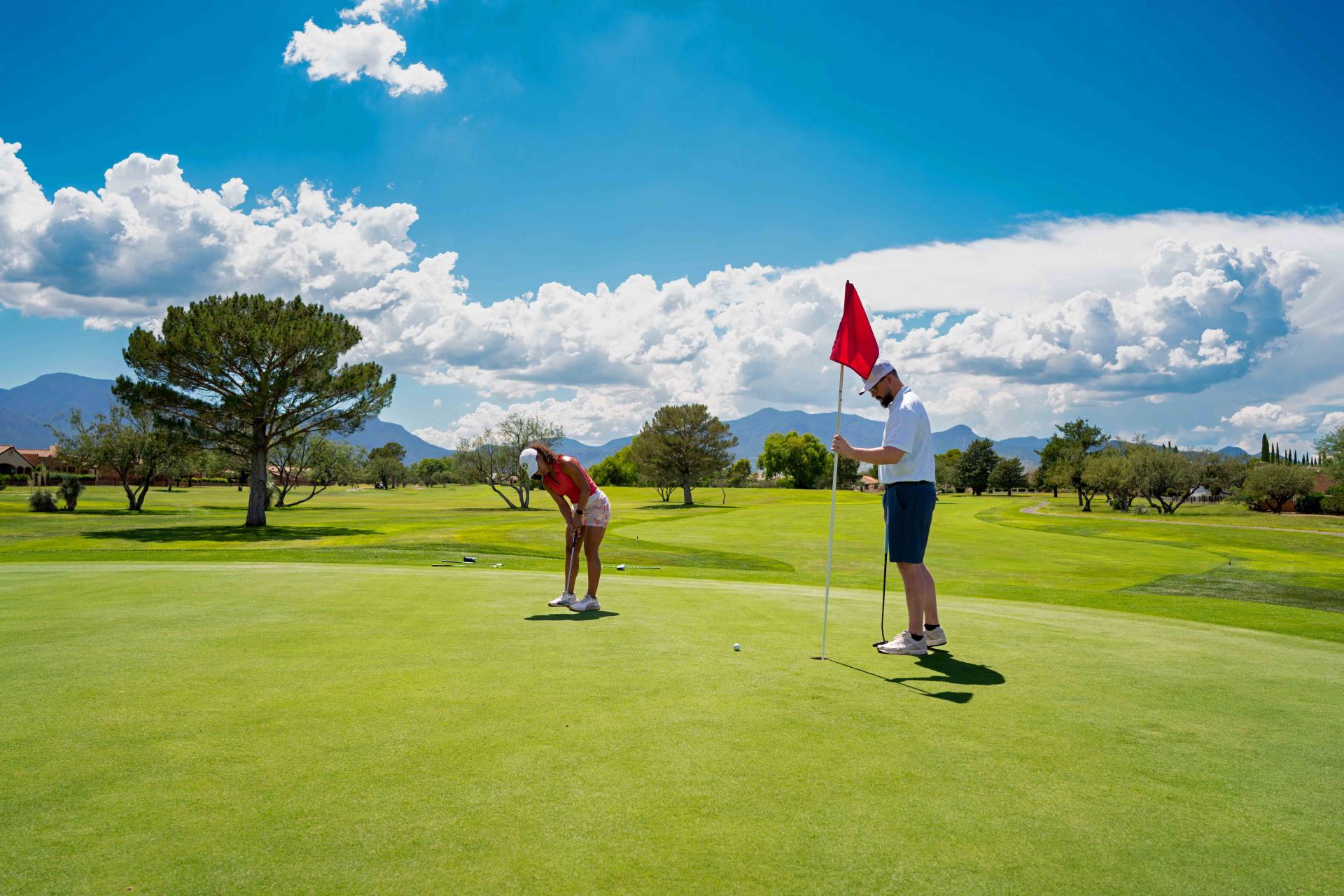 woman putts on a green while man holds flag