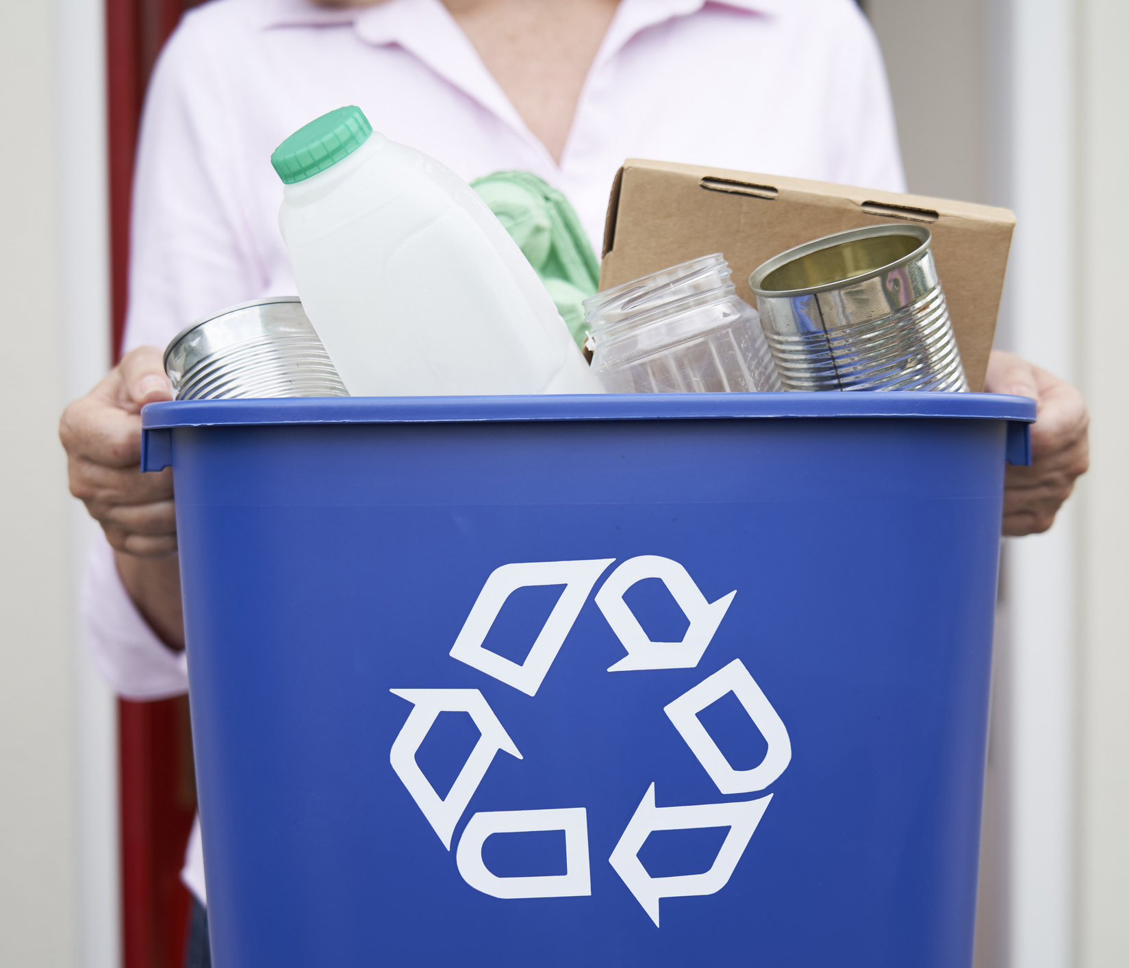 A person holding a recycling bin full of recyclables. 