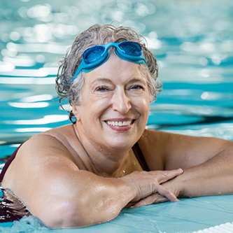 Lady swimmer smiling and resting on the side of the swimming pool