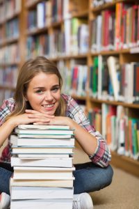 Caucasian girl sitting down leaning forward on a pile of books.